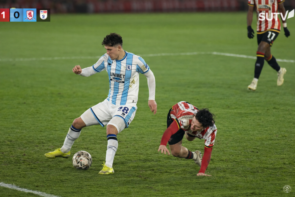 Pronostico Championship (settimana 9–16 febbraio 2026): Sheffield United vs Middlesbrough 1 Pronostico Championship (settimana 9–16 febbraio 2026): Sheffield United vs Middlesbrough. Azione di gioco con dribbling e contrasto a centrocampo; un giocatore in maglia bianca e azzurra protegge il pallone mentre l’avversario in rosso e bianco cade, formato 16:9 HD.